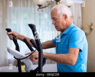 Old man using elliptic trainer at home Stock Photo