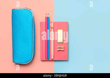 Top view of pencil case with pink notepad and school supplies with space for text over blue and pink background. Back to school concept Stock Photo