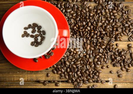 Flat design top-down showing red ceramic cup on saucer with scattered coffee beans on wooden table Stock Photo