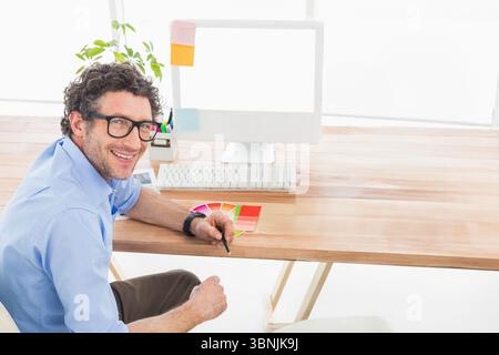 Color swatch booklet lying beside blank computer monitor on wooden desk under bright window light Stock Photo