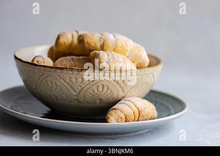 From above, a rustic ceramic bowl filled with freshly baked homemade croissants is placed on a matching plate, showcasing the delicious pastries duste Stock Photo
