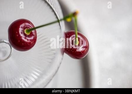 From above, a vibrant ripe cherry rests beautifully on a textured glass surface, highlighting its glossy red skin and fresh green stem, creating a viv Stock Photo