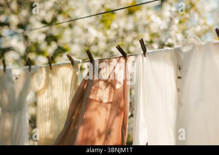 Sunlit clothes sway gently on a outdoor clothesline, casting soft shadows against a backdrop of blurred foliage. The fresh air and warm sunlight depic Stock Photo