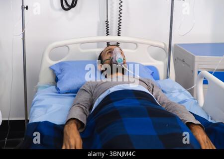 A patient lies in a hospital bed using an oxygen mask for respiratory support. Various medical devices and IV lines are visible, illustrating a clinic Stock Photo