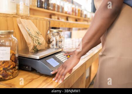 An organic supermarket clerk stands at a counter, managing goods in an eco-friendly bulk store. The setup includes a scale and various organic product Stock Photo