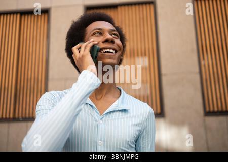 A joyful non-binary person talks on the phone outdoors, symbolizing identity, freedom, and pride. The image highlights diversity and inclusivity in a Stock Photo