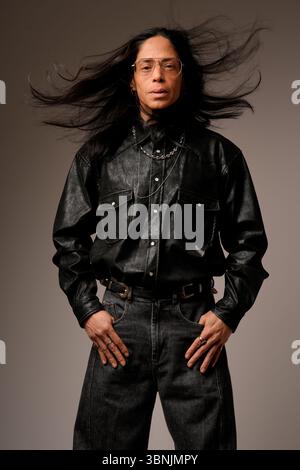 Portrait of a Latin man wearing glasses and a black leather shirt. His long hair is dramatically blown by the wind, adding dynamic movement to the ima Stock Photo