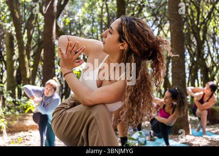 A group of people practicing yoga in the serene setting of a forest, combining the tranquility of yoga poses with the invigorating experience of hikin Stock Photo