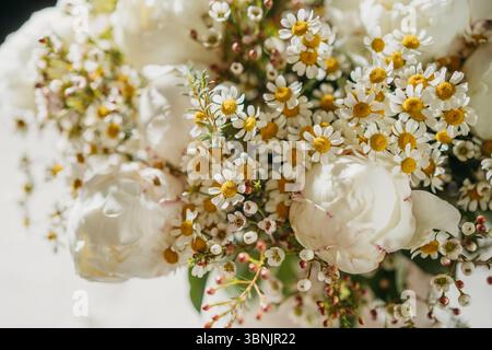 A close-up of a charming bouquet, featuring white peonies, daisies, and wildflowers, illuminated by soft light. Perfect for spring, weddings, and show Stock Photo