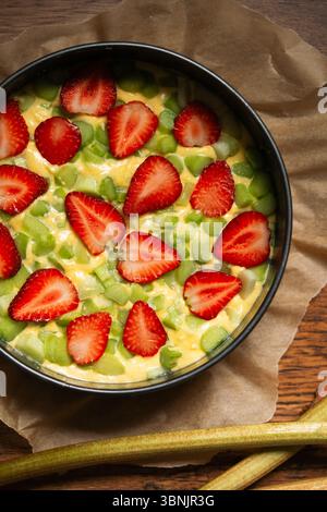 Freshly homemade strawberry rhubarb cake placed on baking paper, showcasing a vibrant mix of sliced strawberries and rhubarb on a creamy batter, ready Stock Photo