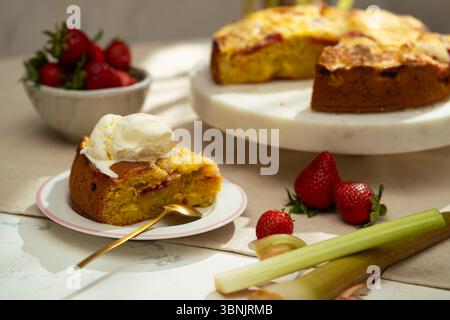 A delicious homemade strawberry rhubarb cake topped with a scoop of creamy vanilla ice cream, served on a decorative plate. Fresh strawberries and rhu Stock Photo