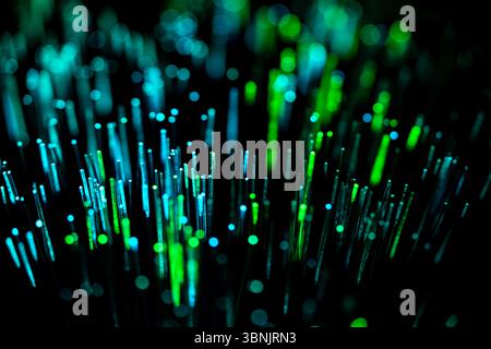 A mesmerizing display of illuminated optical fiber strands, showcasing vibrant green and blue hues against a dark background, symbolizing modern techn Stock Photo