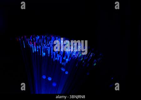 Close up of glowing optical fiber strands emitting blue and multicolored light against a dark background, showcasing the beauty and technology of data Stock Photo