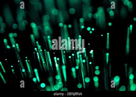 A mesmerizing display of glowing optical fibers, radiating a vibrant green light against a dark backdrop. Represents high speed data transmission and Stock Photo