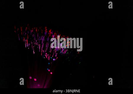 Close up of optical fiber illuminated with vibrant colors against a dark background, showcasing the intricate patterns and technology behind fiber opt Stock Photo