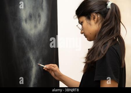 A young Indian woman artist focuses intently on her canvas, creating a captivating masterpiece. Her concentrated expression highlights her passion and Stock Photo