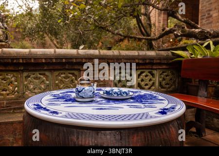 A traditional Vietnamese tea set sits elegantly on a decorative blue and white table in a tranquil outdoor setting. The surrounding greenery and rusti Stock Photo