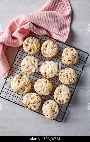 From above, freshly baked scones with chocolate drops rest on a cooling rack, complemented by a textured pink cloth, offering a rustic, homemade feel. Stock Photo