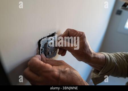 Elderly man performing DIY tasks at home, carefully installing or repairing a light switch. The image captures concentration and skill during a home i Stock Photo