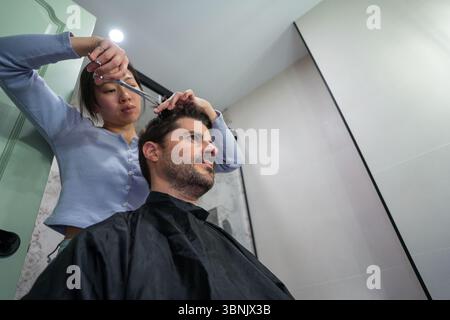 A couple enjoys quality time together as one gives the other a haircut in their modern bathroom. This shared ritual highlights personal care and relat Stock Photo