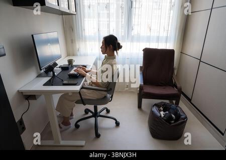 A young professional is using a robot assistant in a modern home workspace. The setup includes a mechanical keyboard and a robot interface, illustrati Stock Photo