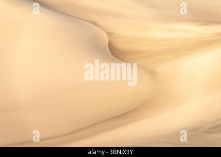 A stunning display of golden sand dunes showcasing intricate swirling textures. The softly contoured surfaces create a mesmerizing natural pattern und Stock Photo