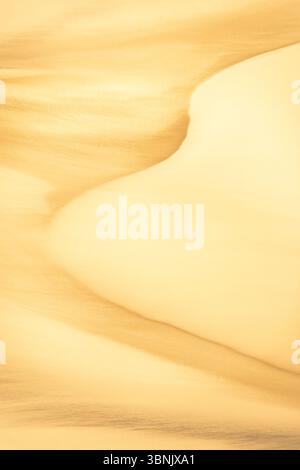 A captivating image of golden sand dunes highlighting intricate textures and patterns. The soft curves and subtle gradients create a mesmerizing natur Stock Photo