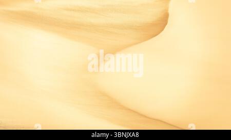 A captivating view of golden sand dunes showing intricate textures and gentle curves, bathed in warm sunlight. The natural patterns evoke a sense of t Stock Photo