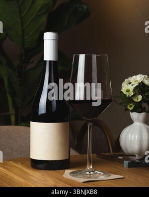 A wine bottle and glass sit elegantly on a wooden table in a restaurant. The setting is enhanced by a white flower vase, creating a sophisticated dini Stock Photo