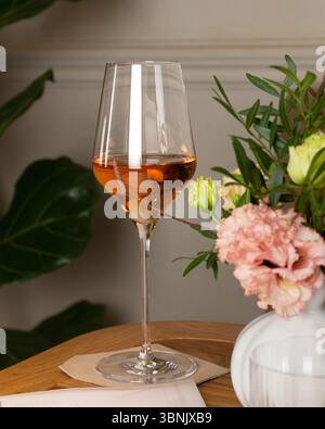 A glass of wine elegantly placed on a wooden table beside a vibrant floral arrangement, creating a sophisticated atmosphere in a beautifully decorated Stock Photo