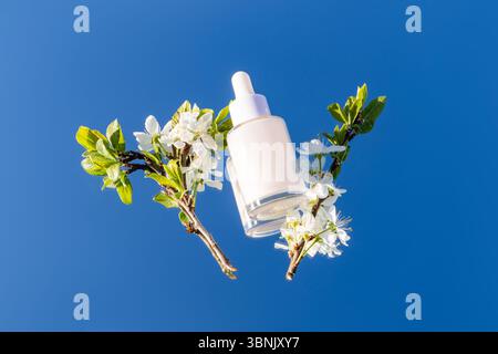 A serene composition featuring a serum bottle elegantly placed among blooming spring flowers against a clear blue sky, evoking freshness and natural b Stock Photo