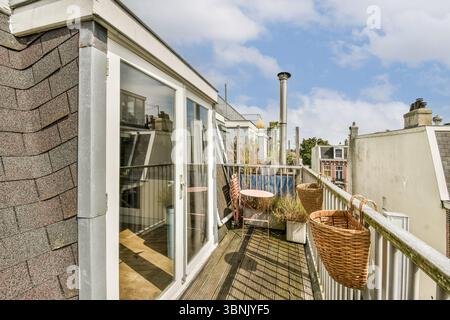 A charming urban rooftop terrace featuring wicker baskets and a small round table with chairs. Surrounded by city buildings and open sky, it offers a Stock Photo