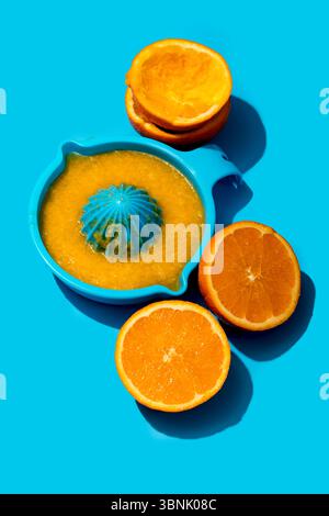 Top view of orange juice in a blue squeezer with halved oranges on a bright blue surface, showcasing a refreshing summer beverage setup. Stock Photo