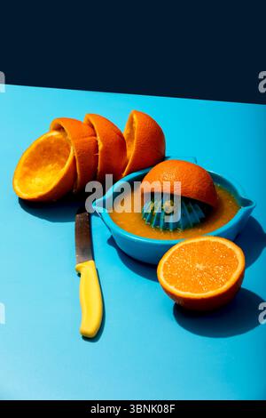 From above of a vibrant scene with freshly squeezed orange juice in a blue bowl, surrounded by sliced oranges and a yellow-handled knife, all set on a Stock Photo
