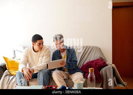 A young Arab man is seated on a cozy couch, engaging in his daily routine while sharing an interactive moment with a friend, surrounded by a warm and Stock Photo