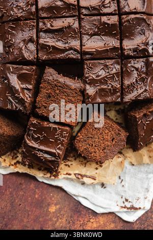 Close-up of chocolate cake squares with glossy frosting and chocolate sprinkles arranged on parchment paper. Perfect for dessert ideas and sweet indul Stock Photo