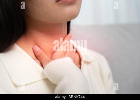 Asian woman put on neck due to a sore throat. female tonsillitis causes a inflammation. treated by taking water, taking antibiotics, consult a doctor, Stock Photo