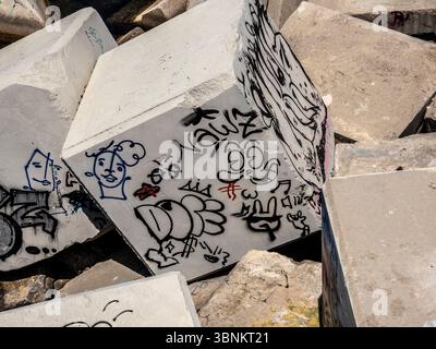 Graffiti and street art cover the concrete blocks of the sea defence breakwater in the Port of Barcelona, creating an urban, abstract texture. Spain. Stock Photo
