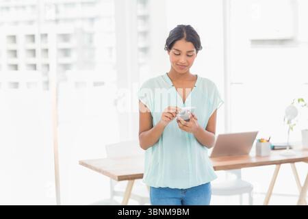 Laptop resting on wooden desk with smartphone, colored pencils, books and potted plant near window Stock Photo