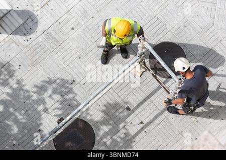 Aerial view of two construction workers assembling scaffolding on a city street sidewalk Stock Photo