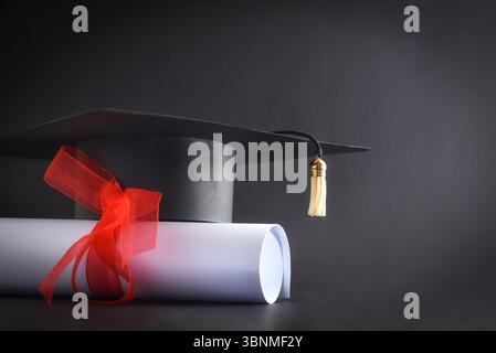 Academic cap and diploma with red ribbon isolated on black background. Front view. Stock Photo