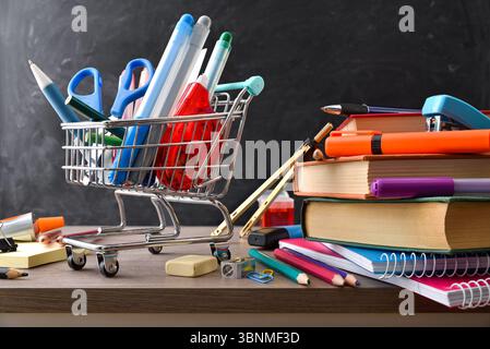 School supplies shopping concept with a mini shopping cart filled with pencils and other various school tools and materials around on a wooden table a Stock Photo