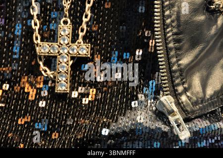Costume jewelry cross with glittering stones on black knitted sweater with sequins with faux leather jacket Stock Photo