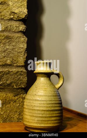 Close-up of a single clay vase on a fireplace mantle corner against shadows on an interior wall. Stock Photo