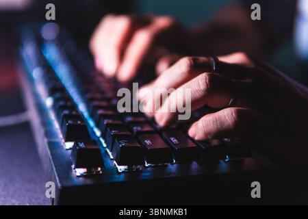 Close-up hands typing on a mechanical keyboard with LED backlight in a dark room. Stock Photo