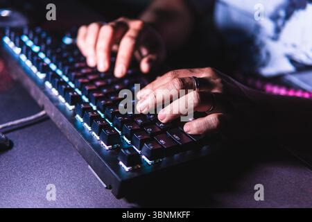 Close-up hands typing on a mechanical keyboard with LED backlight in a dark room. Stock Photo
