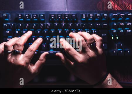 Close-up hands typing on a mechanical keyboard with LED backlight in a dark room. Stock Photo