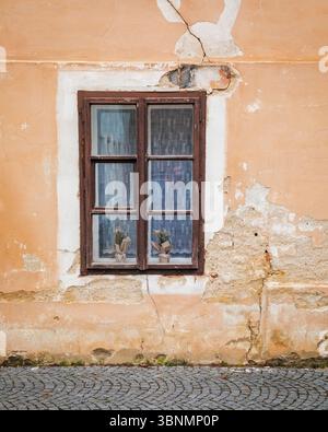 Rustic window set in a cracked, aged wall with urban pavement below Stock Photo