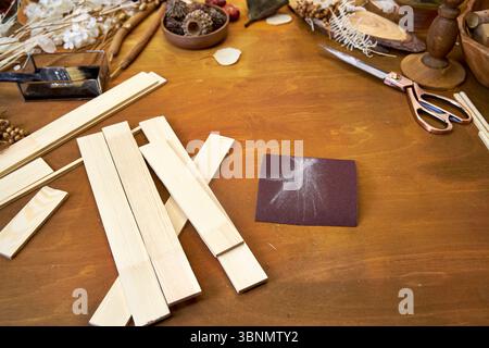 Woodworking workspace with light wooden planks, sanding paper, dried flowers, and tools. DIY project preparation for a natural decorative collage or Stock Photo
