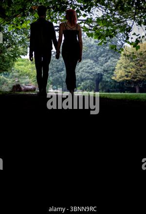 A couple walks hand-in-hand down a path in a park. Stock Photo